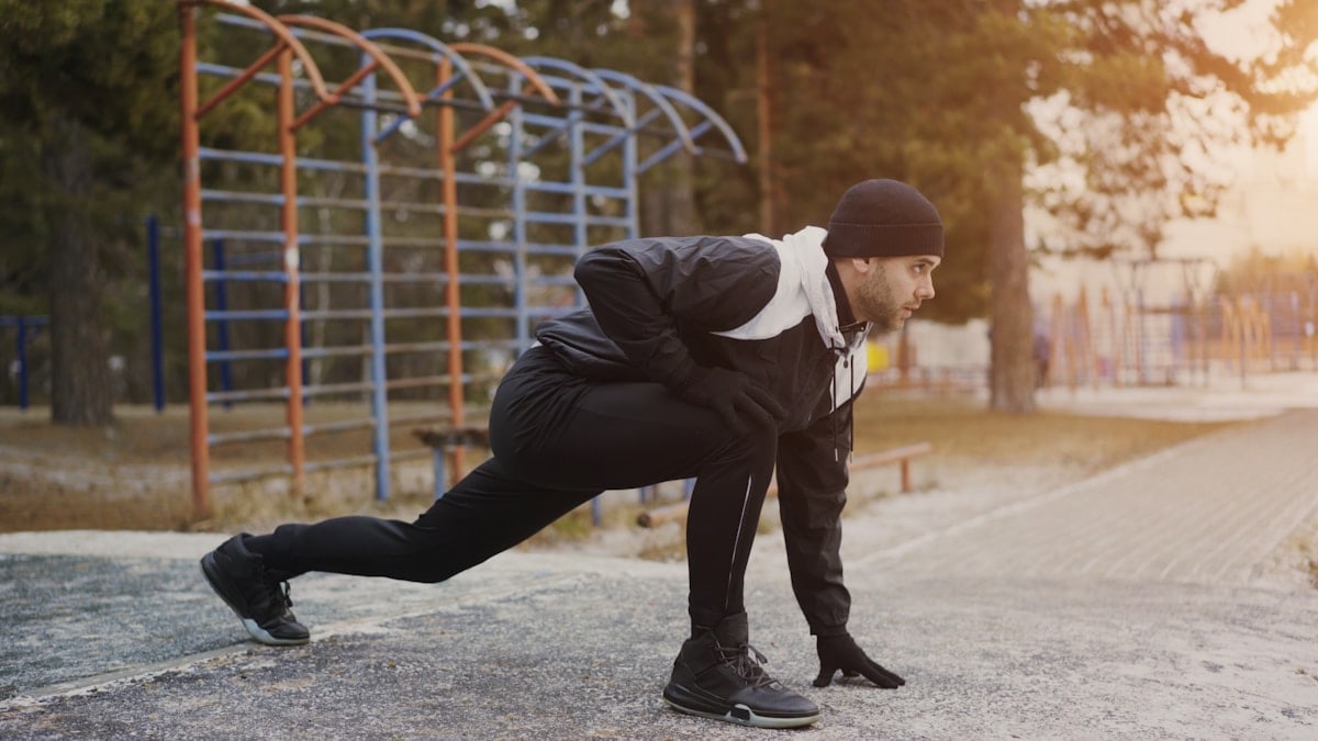 Young man runner doing stretching exercise preparing for morning workout and jogging in winter park